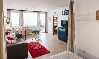 A modern room with a cozy living area and a small dining space.  
Large windows provide plenty of daylight and a welcoming atmosphere.