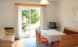 A cozy dining area with a table and chairs. Large windows provide a view of the garden.