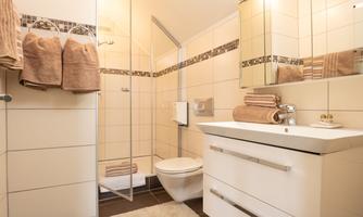 A modern bathroom with a clean, minimalist design. It features a shower, a modern sink, and soft towels.