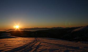 A beautiful sunrise over snow-covered mountains. The tracks in the snow lead into the distance.