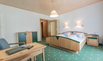 A cozy bedroom with a double bed and two nightstands. The room has a desk and a green carpet.