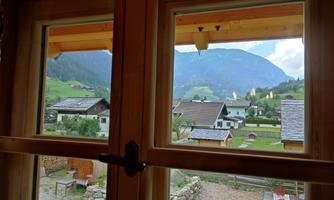A view from the window of a beautiful valley with green meadows and mountains in the background. The surroundings feature traditional houses in a tranquil rural atmosphere.