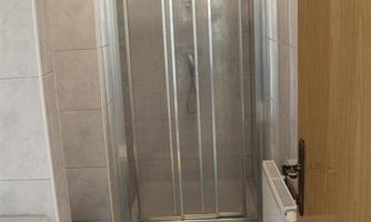 A modern bathroom with a shower, a toilet, and a sink. The room is brightly tiled and well-equipped.