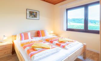 A bright bedroom with a large bed and colorful bedspreads. Through the window, there is a beautiful view of greenery.