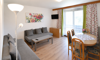 A modern living room with a cozy sofa, a dining table, and chairs for up to 7 people. Large windows provide plenty of light and a friendly atmosphere.