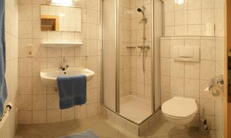 A modern bathroom with tiled walls and a shower cabin. There is a sink, a toilet, and a blue towel on the floor.