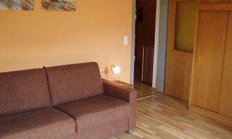 A simple living room with a brown couch and a small table. The walls are painted orange and there is a cabinet and a glass door transition in the background.