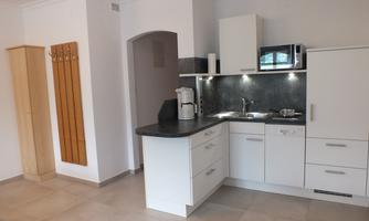 A modern kitchen with white cabinets and a dark countertop. In the background, there is a microwave and a coffee maker.
