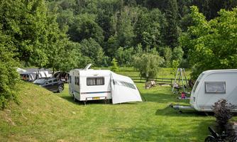 A campsite with caravans on a green meadow.  
Surrounded by trees and a peaceful landscape.