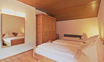 A cozy bedroom with three beds and wooden paneling. A mirror reflects the calm atmosphere of the room.