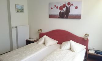A simple room with two single beds and white bed covers. A modern painting with red and black elements hangs on the wall.