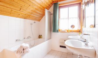 A modern bathroom with a bathtub and two sinks. The wooden ceiling and the window create a bright, inviting atmosphere.
