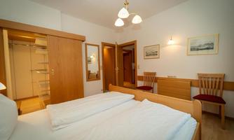 A cozy hotel room with two beds and wooden furniture. There is a wardrobe, two chairs, and soft lighting.