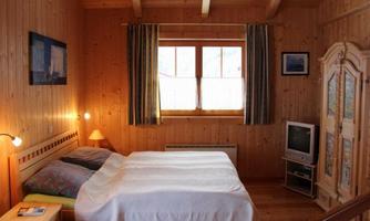A cozy bedroom with wooden paneling. There is a large bed, a television, and a window with curtains.