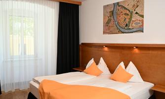 A modern hotel room with a double bed and orange cushions. A piece of art depicting a city map hangs on the wall.