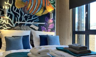 A stylish bedroom with a colorful mural of fish and corals. The bed is invitingly decorated with fresh towels and cushions.