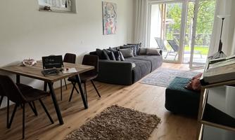 A modern living room with a cozy sofa and a dining table. Large windows let in plenty of light and offer a view of the outdoors.