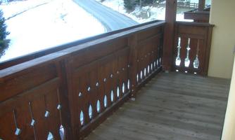 A quiet wooden balcony with traditional decorations. In the background, a snow-covered landscape and a winding road can be seen.