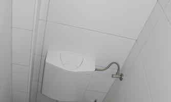A simple bathroom with a white toilet and a white wall.  
There is a toilet paper holder on the floor and the floor is tiled.