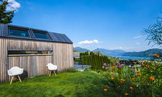 A modern wooden house with a beautiful garden. In the background, you can see a clear lake and a picturesque mountain landscape.