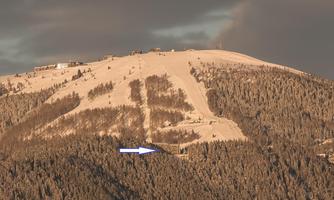 A snow-covered mountain landscape with a clear sky. At the summit, facilities and slopes are visible.