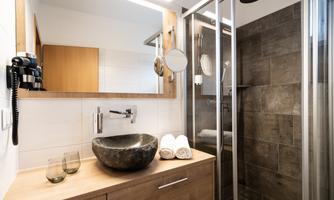 A modern bathroom with a shower and an elegant stone sink. The walls are designed with light and dark tiles.
