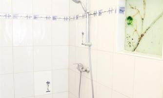 A bright shower cabin with white tiles and a modern shower fixture. On the wall, there is a window with a green pattern.