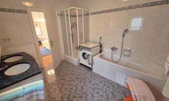 A modern bathroom with a bathtub, shower, and washing machine. The walls are tiled and the floor has an elegant pattern.