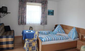 A simple room with two beds and a seating area. There is a table and a television on the wall.