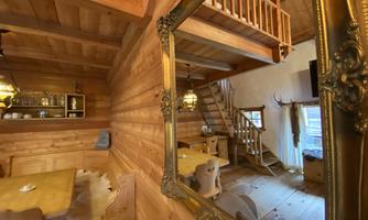 A cozy chalet with wooden paneling and warm light. In the background, there is a staircase and rustic furnishings.
