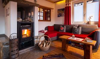 A cozy living room with a modern fireplace and a red couch. On the table are books and decorations, while a warm atmosphere is created through the window.