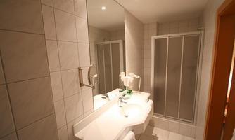 A modern bathroom with white tiles and a large mirror. The shower is separated by a glass partition.