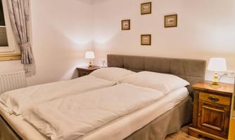 A cozy bedroom with a double bed and warm light. Small pictures hang on the walls, and the floor is made of wood.
