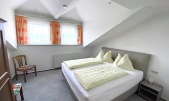 A bright hotel room with two beds and a cozy decor. The room has large windows with colorful curtains and simple wooden chairs.