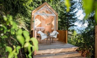 A modern, small wooden house on a terrace amidst green trees. The decor is inviting and offers a view into nature.