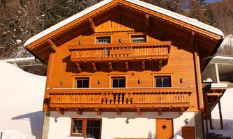 A traditional wooden house with balconies, surrounded by snow. The architecture features a rustic, alpine design.
