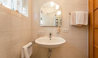 A modern bathroom with a round mirror and a sink. The walls are tiled in light colors and fresh towels are available.