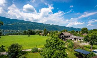 A picturesque landscape with green meadows and mountains in the background. The sky is clear with some white clouds.