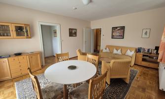 A bright living room with a round table and wooden chairs. There is a sofa, a rug, and subtle wall decorations.