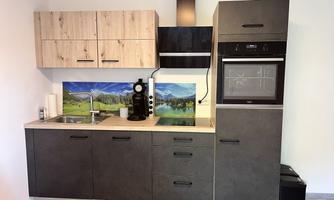 A modern kitchen with wood and dark cabinets. In the background, there is a picture of mountains and a landscape.