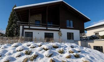 A modern house in winter, surrounded by snow. The blue sky appears clear and sunny.