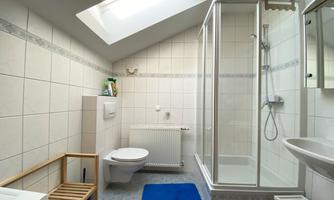 A modern bathroom with a shower, a toilet, and a sink. The room has bright tiles and a window with daylight.
