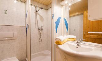 A modern bathroom with a shower and blue dolphins on the walls. There is a sink area with fresh towels in yellow and white.
