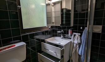 A small bathroom with dark tiles and a yellow floor. There is a shower cubicle and a window view.