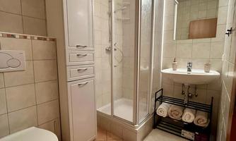 A modern bathroom with a shower, a sink, and a toilet bowl. Towels are neatly stacked on a shelf.