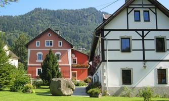 Two houses in a rural setting with green lawns. In the background, the mountains are visible.