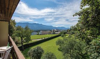 A beautiful view from a balcony of a green meadow and hills in the background. Above the landscape horizon, some clouds can be seen in the blue sky.