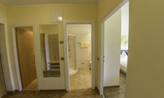 A bright room with yellow walls and wooden flooring. There is a bathroom with a shower and two doors leading to adjacent rooms.