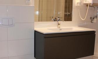 A modern bathroom with a floating sink and a large mirror. There is a toilet and a glass shower enclosure.