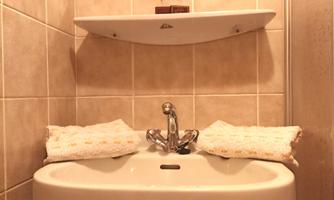 A small bathroom with a sink, a mirror, and a shelf. The walls are tiled and towels are ready.